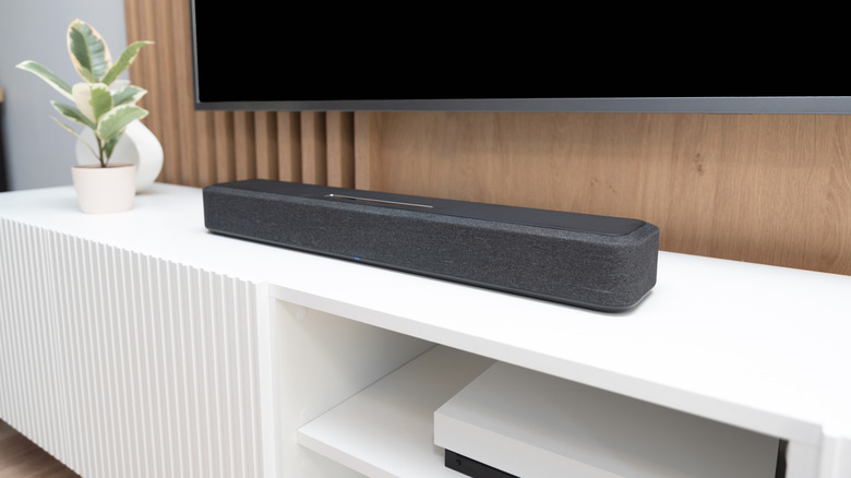 A sleek modern soundbar placed on the front edge of a wooden media console below a television.