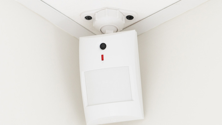 A white motion sensor or camera mounted at the top corner of a room near the ceiling.