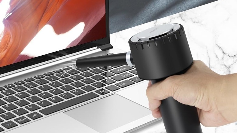 Hand holding an ABVOT Electric Air Duster while cleaning a laptop keyboard.