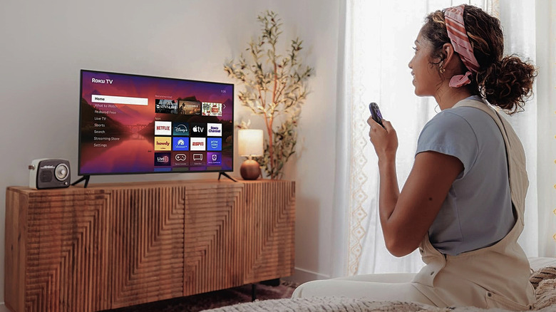 A person watching a movie on a Roku Plus Series TV while sitting comfortably in bed.