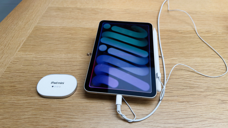 An iPad Mini connected to a charging cable on a wooden surface.