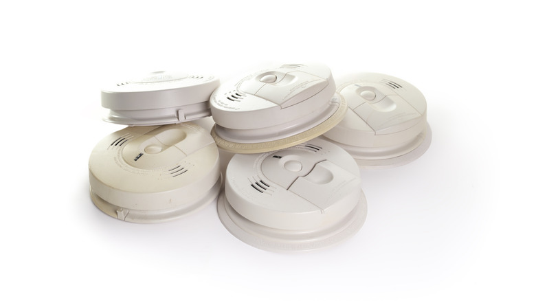 A diverse stack of various smart smoke alarm models and brands.