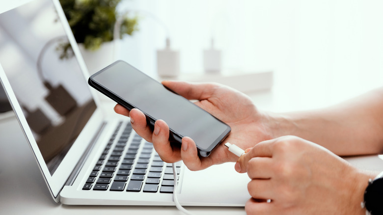 A person connecting a charging cable to an Android smartphone.