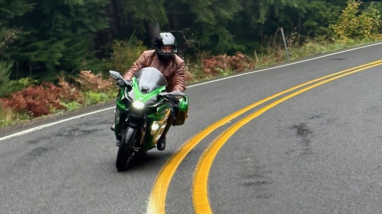 A rider navigating the Kawasaki Ninja H2 SX through a lush forest road.