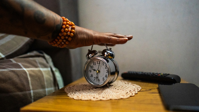 A hand turning off a mechanical twin-bell alarm clock in the morning light.