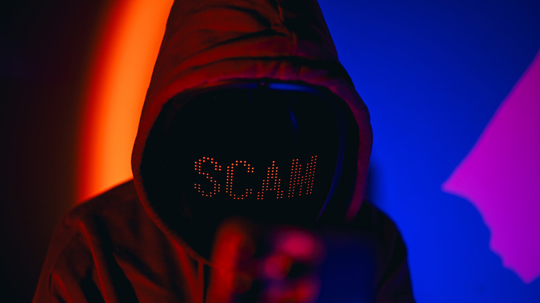 A shadowy figure in a hoodie with the word SCAM superimposed on their face against a vibrant, abstract background.