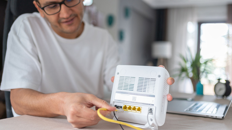 A man connecting an Ethernet cable into the rear port of a home router.