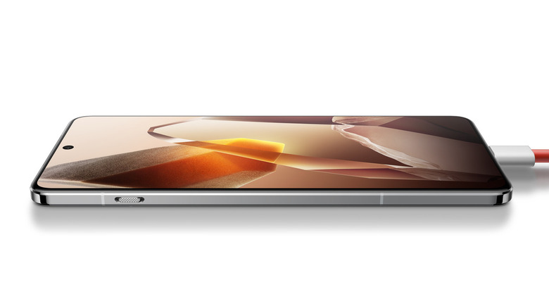 OnePlus 13 smartphone lying on a surface while charging, featuring an abstract crystal-themed screen.