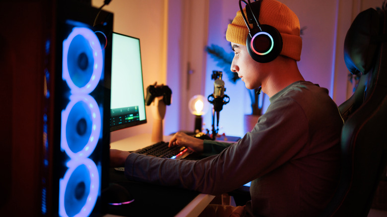 A gamer wearing a headset sitting in front of a finished, glowing gaming PC.