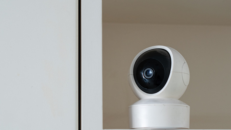A small black security camera positioned between books on a wooden shelf.