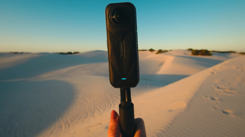 An Insta360 action camera being held up against a backdrop of desert sand dunes.