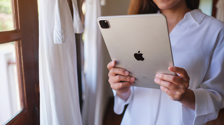 A woman holding and using an Apple iPad in a bright indoor setting.