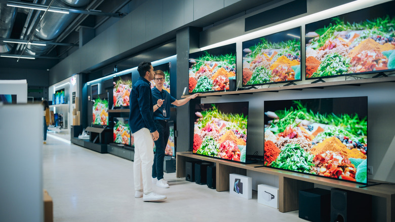 An electronic store employee assisting a customer with various TV options.