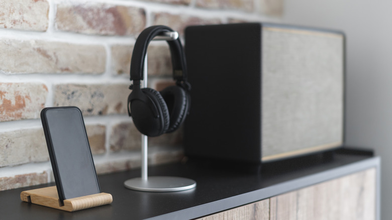 A vintage speaker sitting next to a modern smartphone and wireless headphones on a stand.
