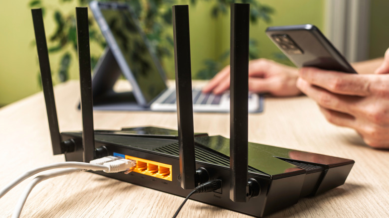 A Wi-Fi router on a wooden workstation with a person working on a laptop in the background.