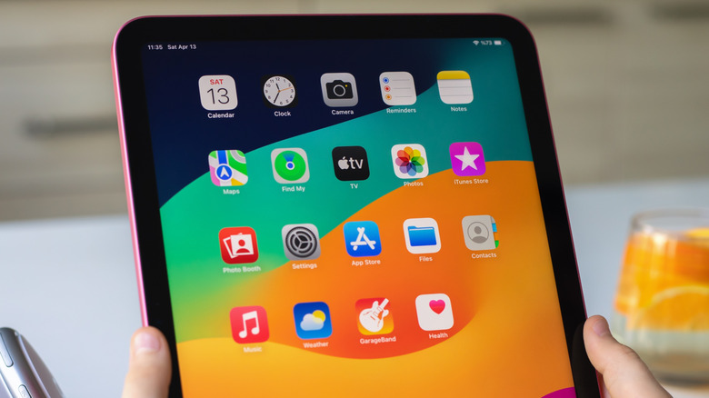 Hands holding an iPad displaying a home screen full of native and professional applications.
