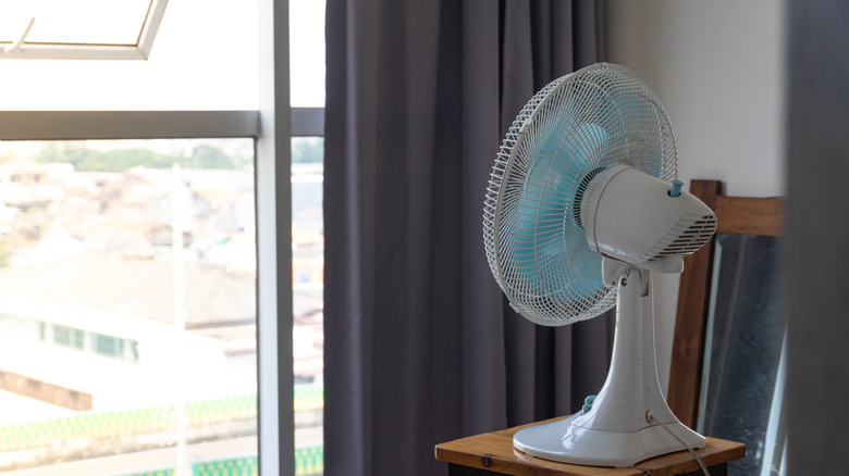A household fan positioned in front of an open window facing outward.