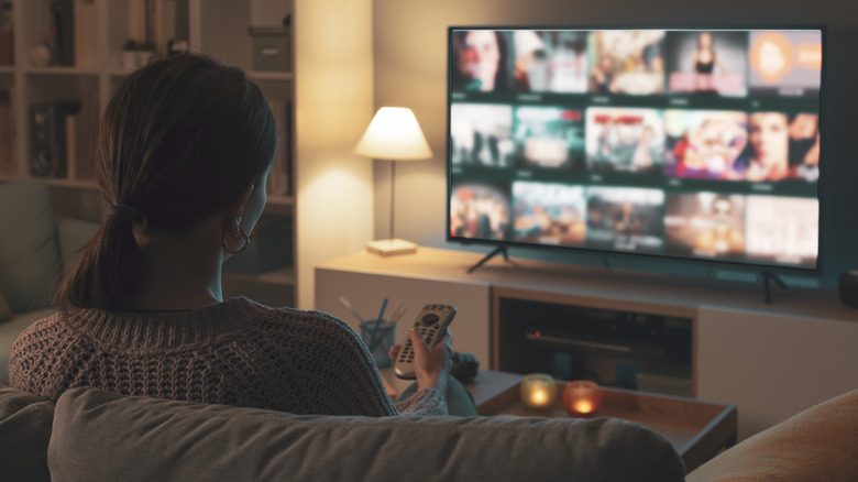 A person sitting on a sofa using a remote control to navigate a television interface.