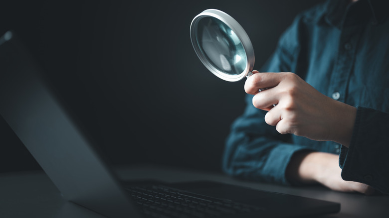 A magnifying glass held over a laptop screen showing tech listings.