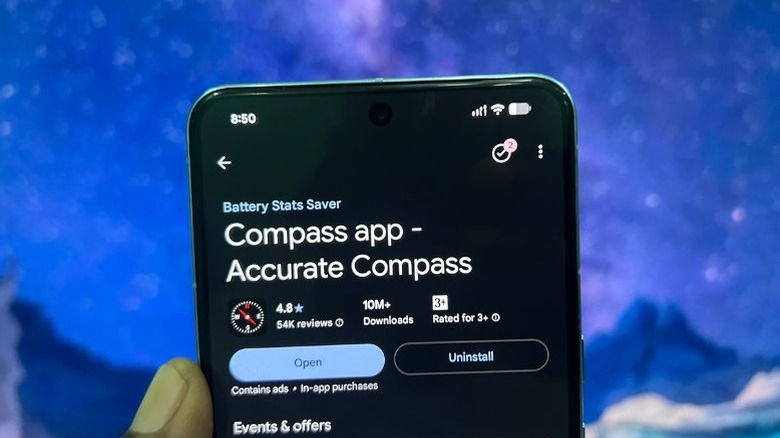 A hand holding a smartphone in an outdoor setting displaying a digital compass app.