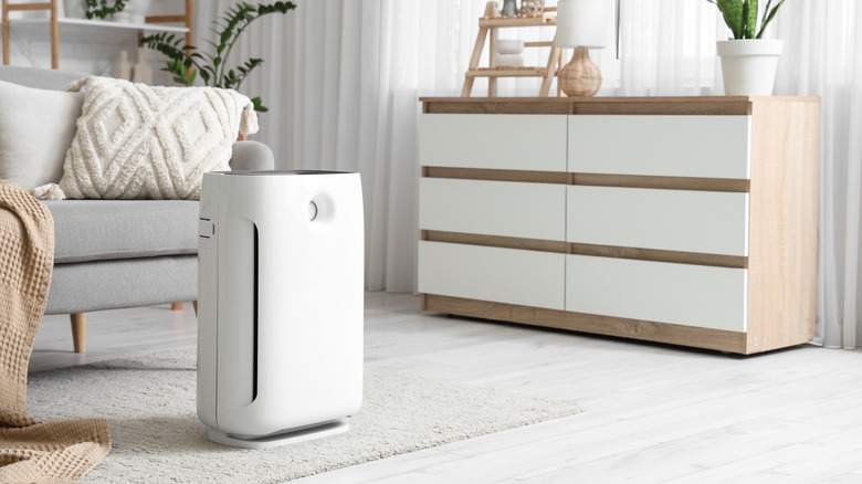 A sleek white air purifier standing in the corner of a bright, modern living room.