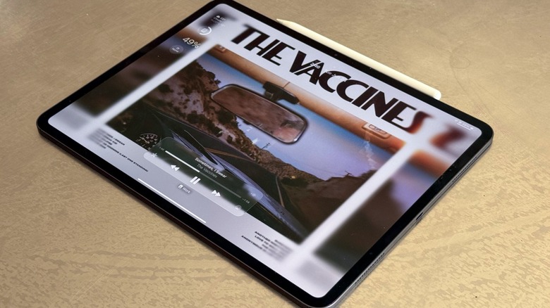 An iPad Pro displaying the iPadOS 26 lock screen with vibrant colors and deep blacks.
