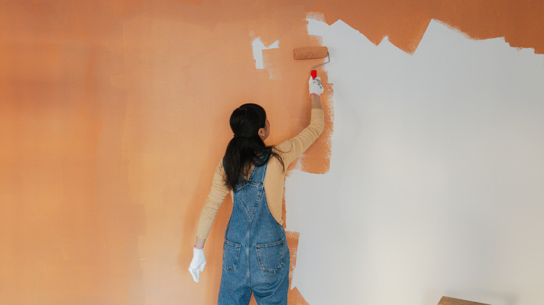 A person painting a wall with bright orange paint using a roller.