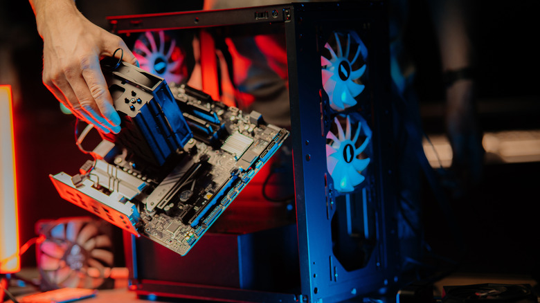 A builder carefully lowering a motherboard with a large air cooler into a PC chassis.