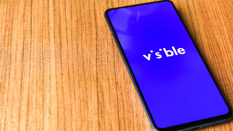 The Visible app running on a smartphone resting on a wooden surface.