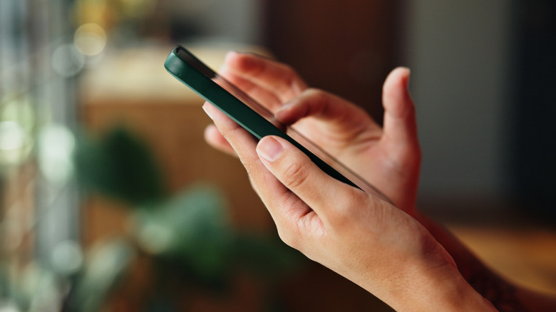 Person holding a smartphone with both hands in a softly lit indoor setting.