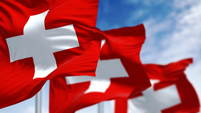 Three Swiss flags in a row against a blue sky.