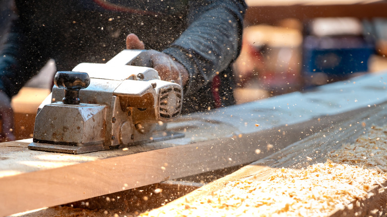 A woodworker using a power tool that is generating a large cloud of fine sawdust.