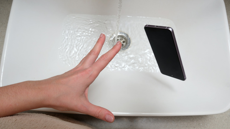 A smartphone being dropped into a water-filled sink.