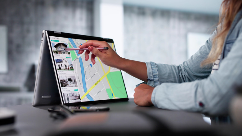 A silver convertible laptop set up in tent mode being used for digital drawing with a stylus.