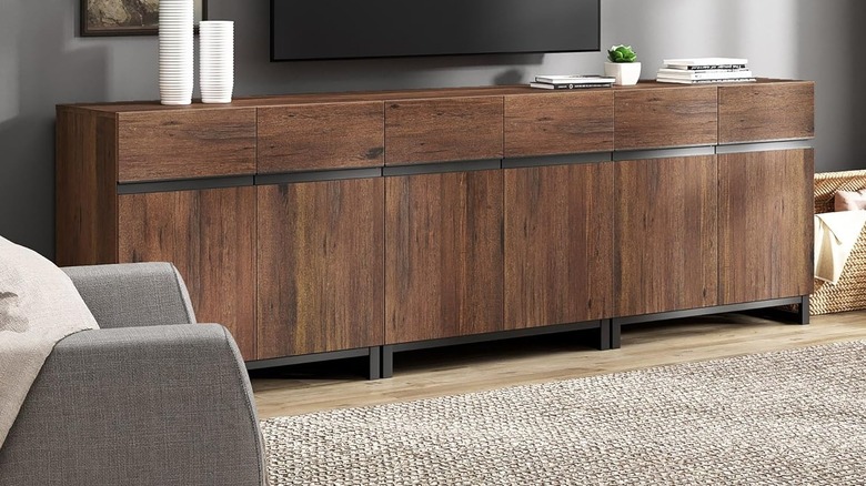 The Wampat Modern TV Stand with a wall-mounted TV above it and decor items on its surface.