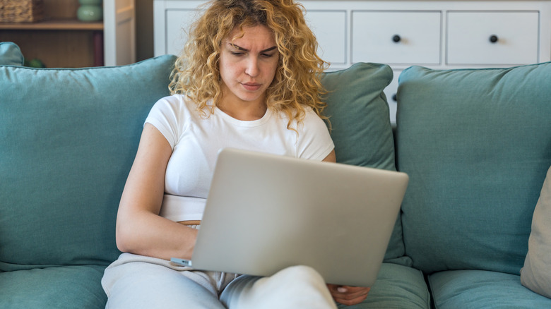 A person attempting to balance a large laptop on their lap while sitting on a sofa.