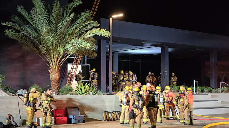 A group of firefighters standing outside a building affected by a battery fire, assessing the situation.