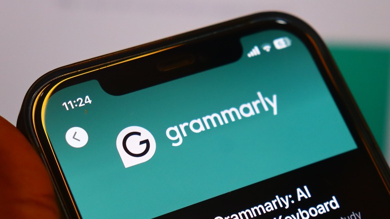 A hand holding a smartphone where a grammar correction app is highlighting and fixing text in an email draft.