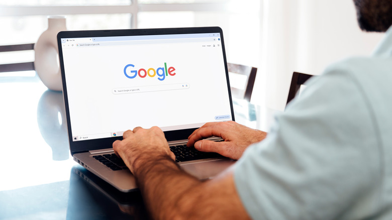 A man focused on typing a search query into a laptop in a bright indoor environment.