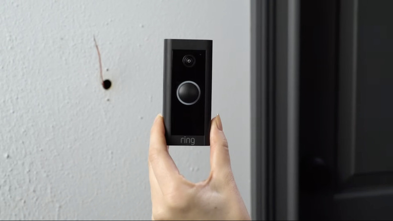 A person's hand holding a black video doorbell camera.