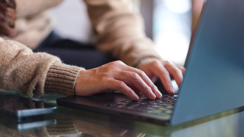 Close-up of a person's hands typing on a modern laptop keyboard.