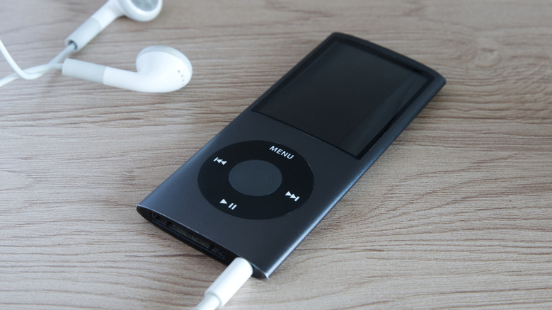 A black 4th-generation iPod Nano lying on a flat surface next to white earbuds.