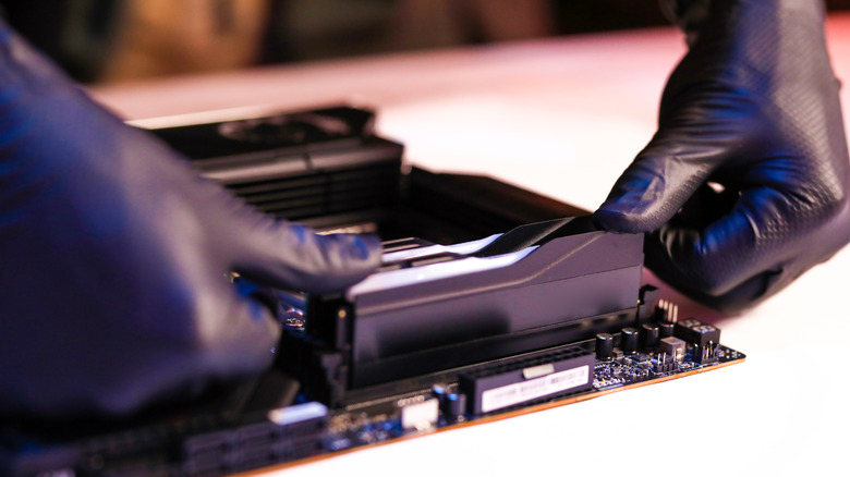 Close-up of a person's hands installing a RAM stick into a motherboard slot.