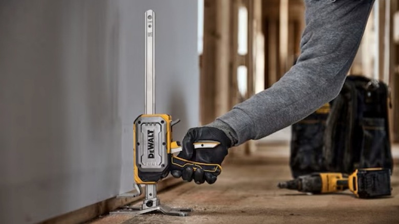 A worker using a DeWalt construction jack to hold a large drywall sheet against a ceiling.