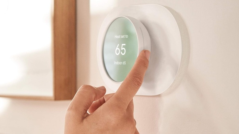 Close-up of a hand adjusting a smart thermostat on a wall.