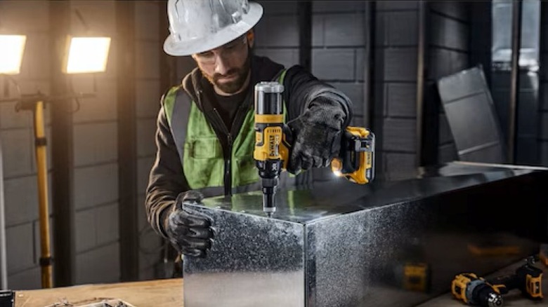 A technician using a DeWalt cordless rivet tool to join sections of metal HVAC ductwork.