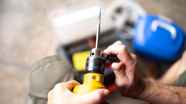A close-up of a person's hand manually rotating a keyless drill chuck to secure a bit.
