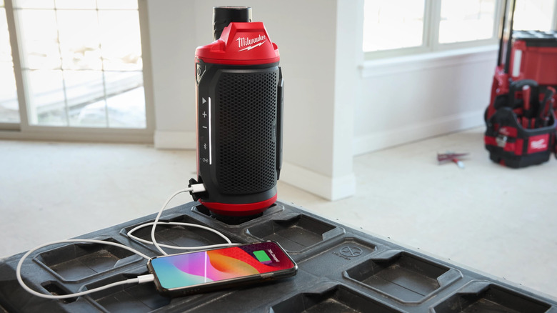 Milwaukee M12 Bluetooth Jobsite Speaker positioned next to a smartphone.