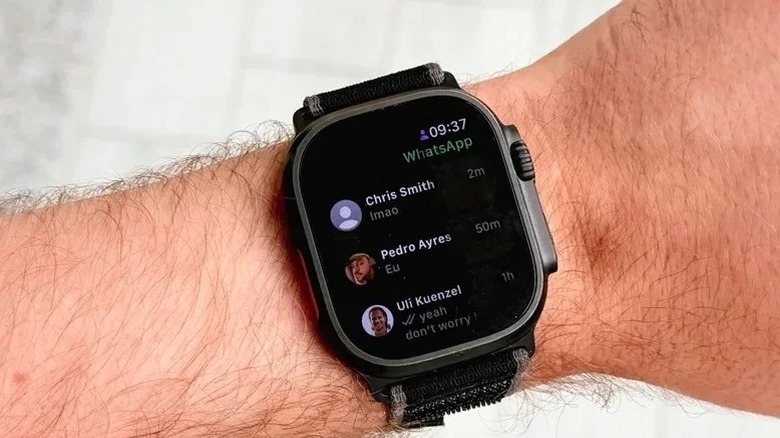 An Apple Watch on a wrist showing the WhatsApp interface with recent chat conversations.