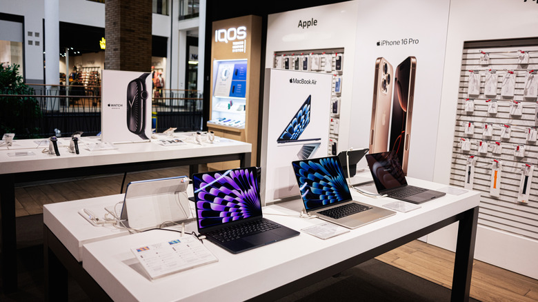 Apple gadgets including MacBooks and iPhones on display at a retail store with promotional pricing context.